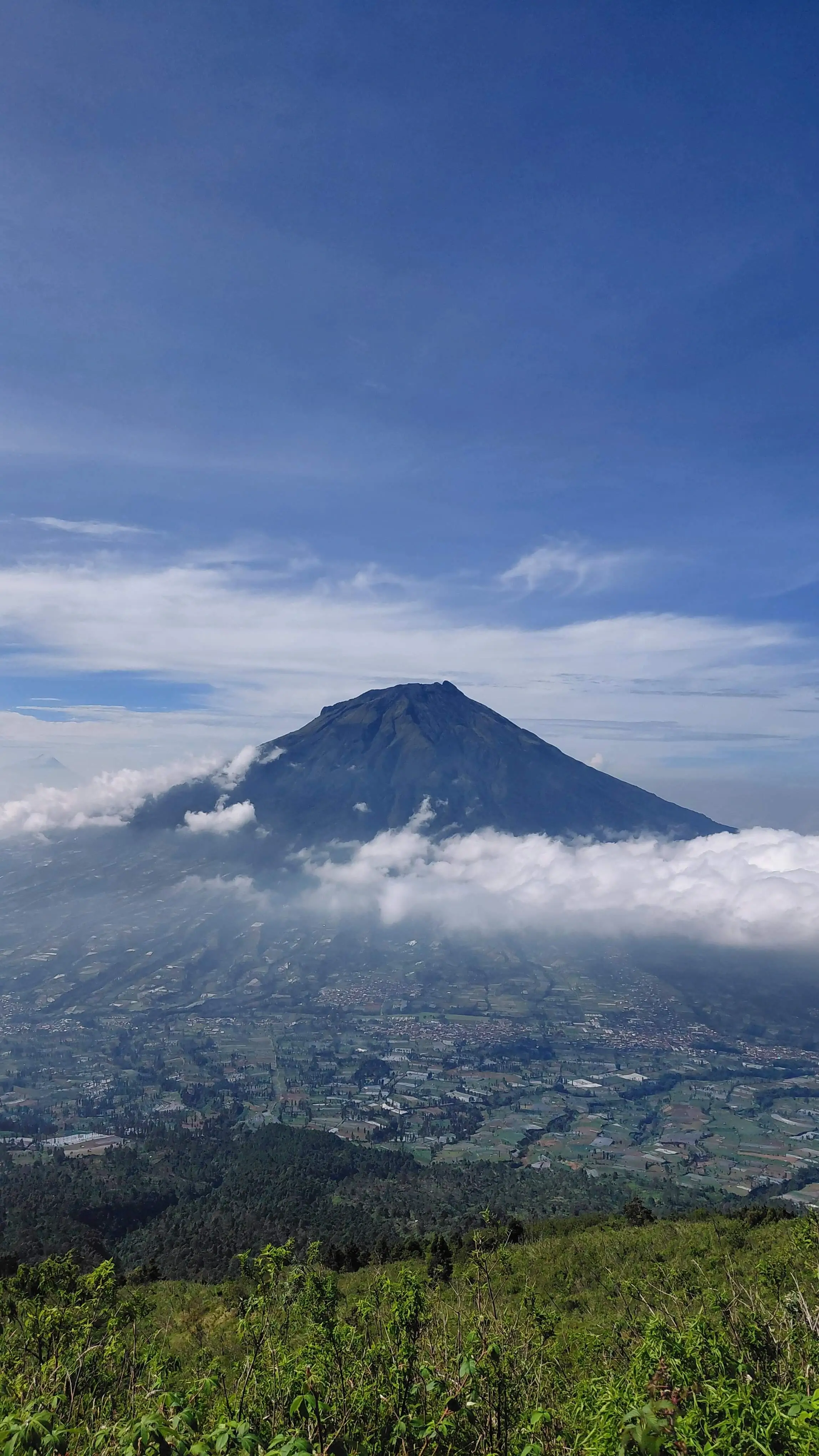 A breathtaking view of Mount Sumbing towering over the clouds as seen from the hiking trail of Mount Sindoro.